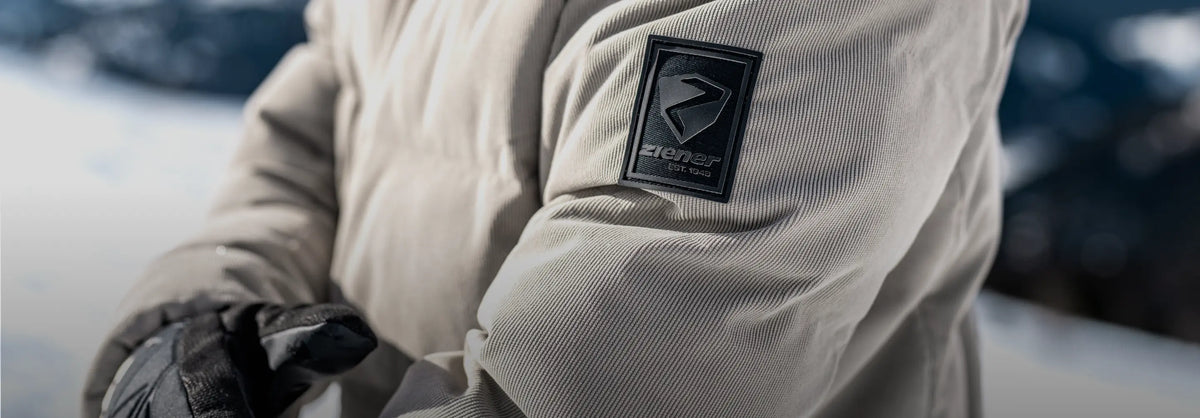 Close-up of the ZIENER logo on the sleeve of a beige ski jacket