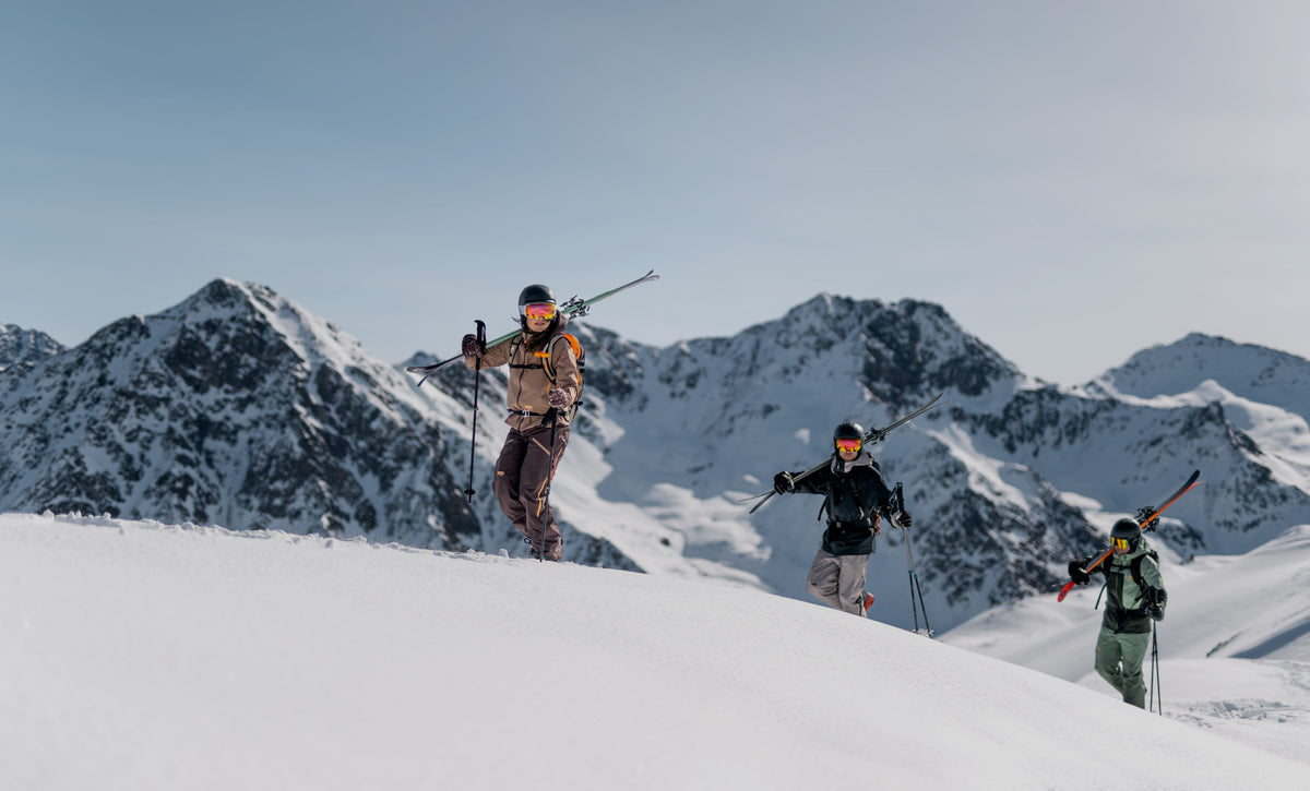 Three skiers carrying their skis across a snowy mountain ridge