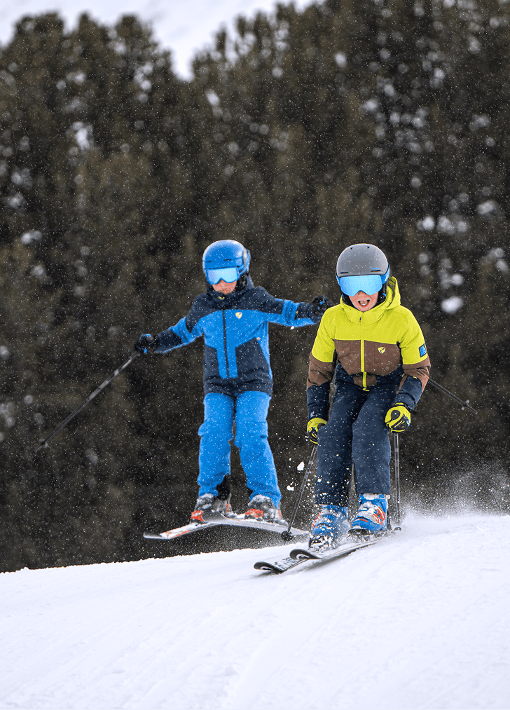 Two children in colourful ski wear skiing side by side