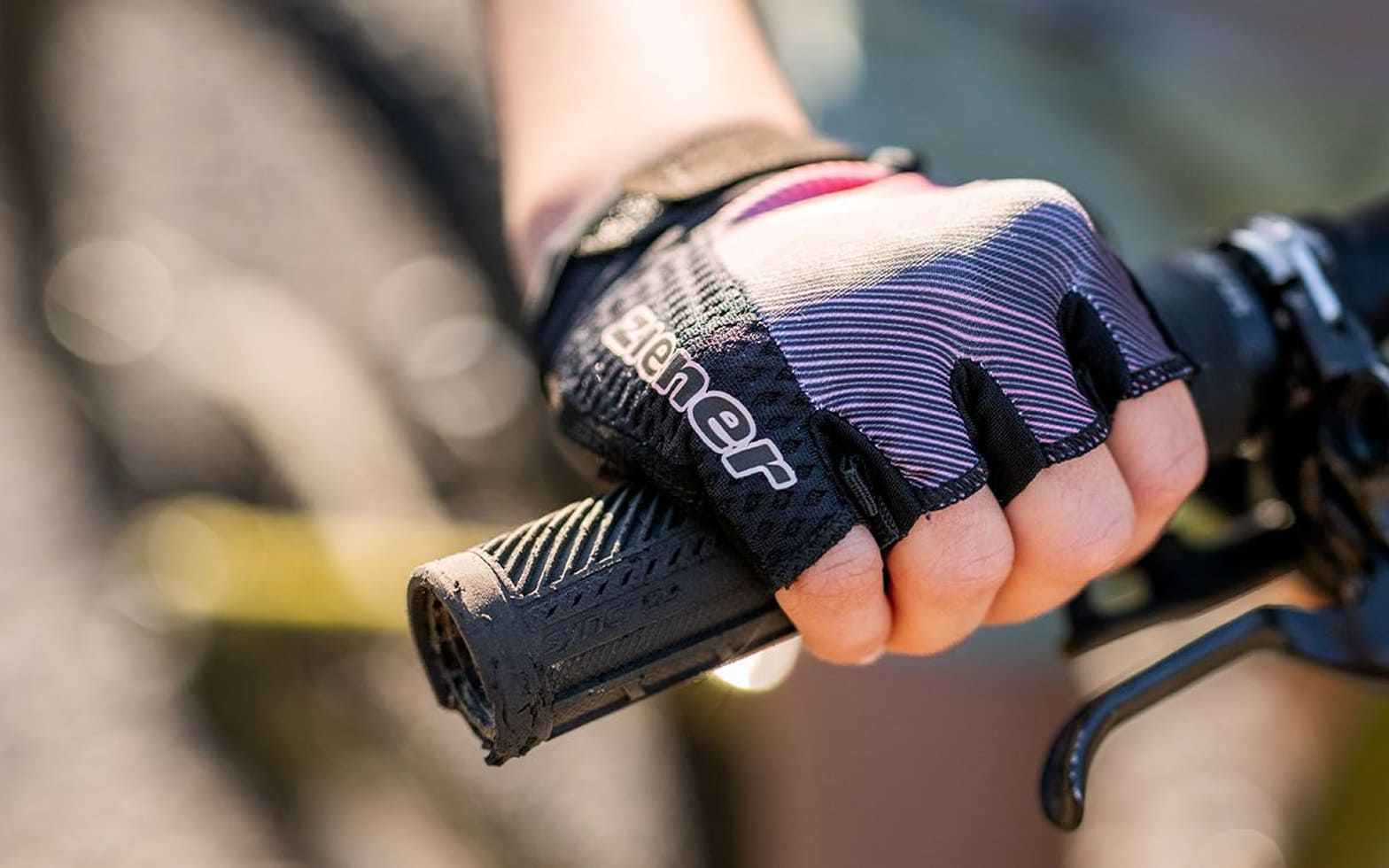 Nahaufnahme einer Hand im dunklen ZIENER Kurzfinger-Bikehandschuh am Lenkergriff