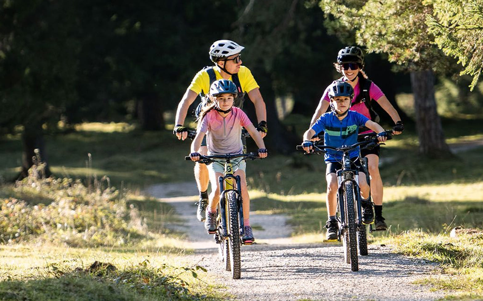 Familie mit zwei Kindern fährt mit Mountainbikes über einen Waldweg