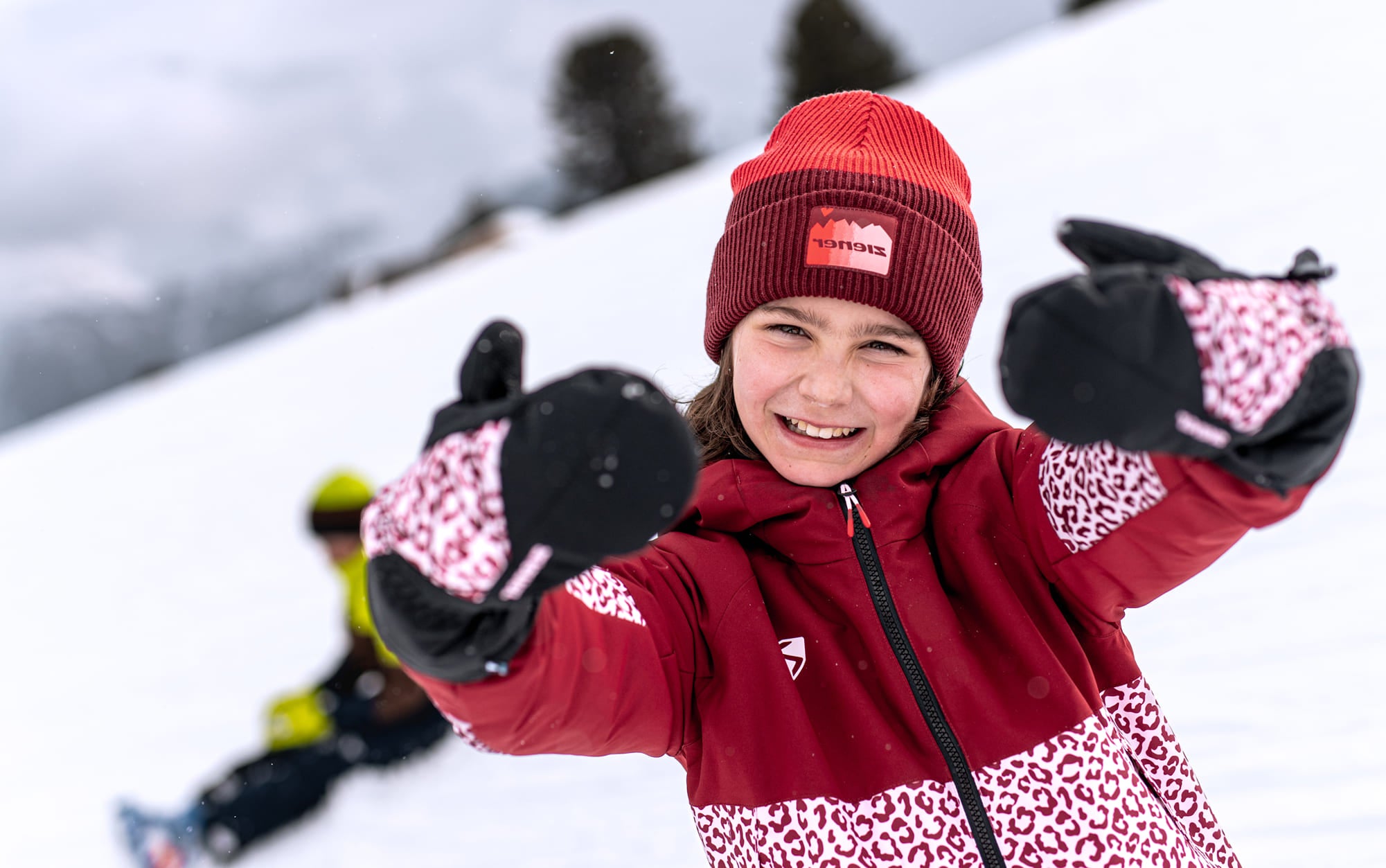 Smiling child in a red beanie showing off black and pink mittens