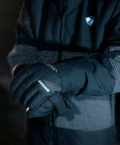 Close-up of black ZIENER gloves against a dark jacket with a reflective ripstop pattern