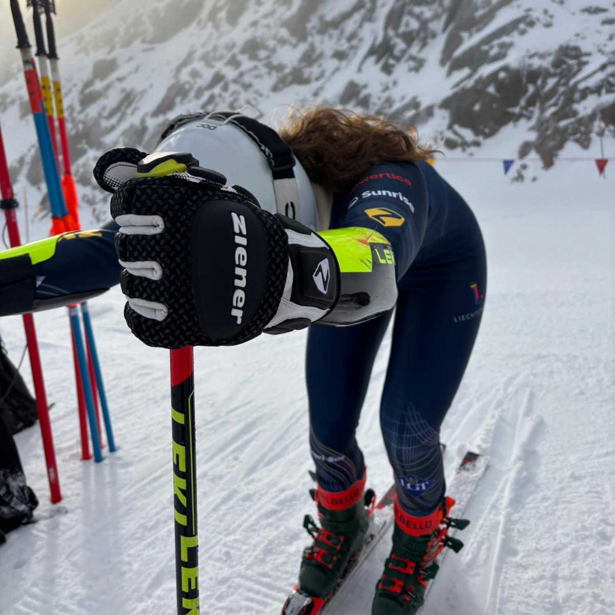 Skirennläuferin im Rennanzug beugt sich nach vorn, im Vordergrund ein schwarzer ZIENER Rennhandschuh